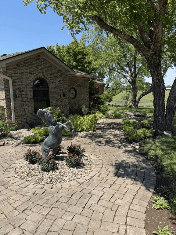 Paver patio with horse statue, flowering plants and lush pathway plantings
