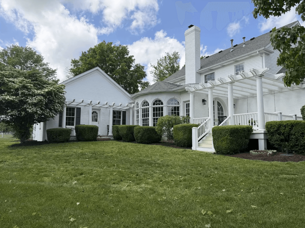 White colonial home with sculpted boxwoods, pergola and clean lawn