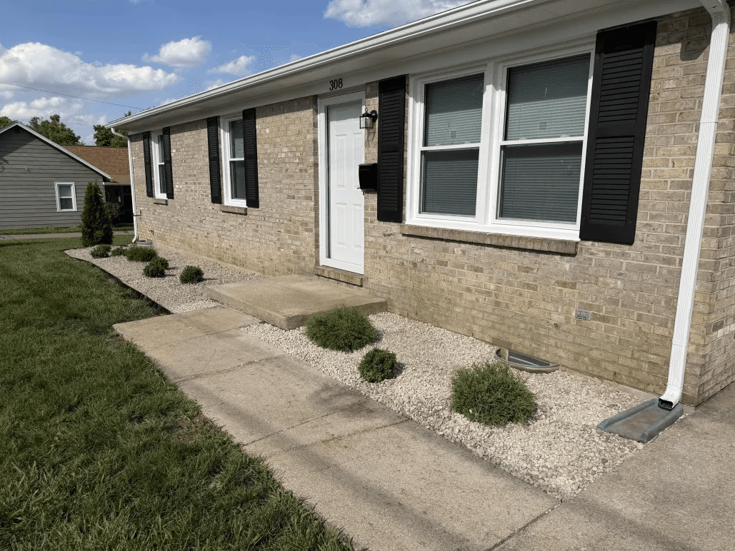 Ranch brick home with river rock bed and shaped evergreen shrubs along front walkway