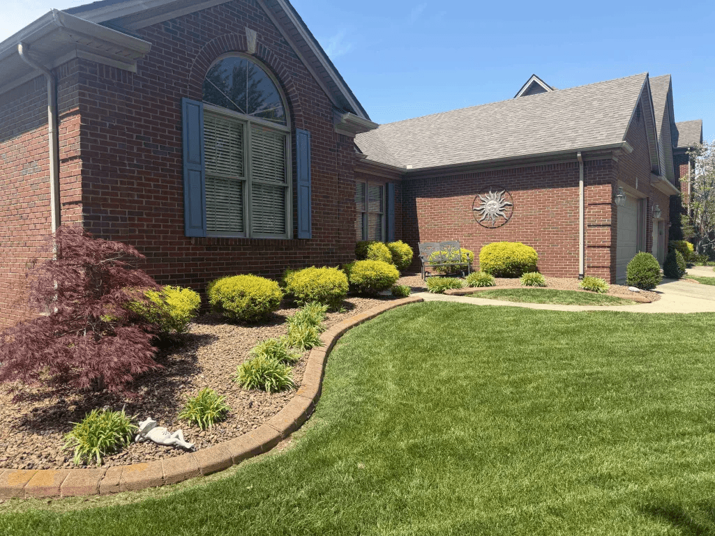 Curved mulch bed with ornamental shrubs and manicured lawn at brick home